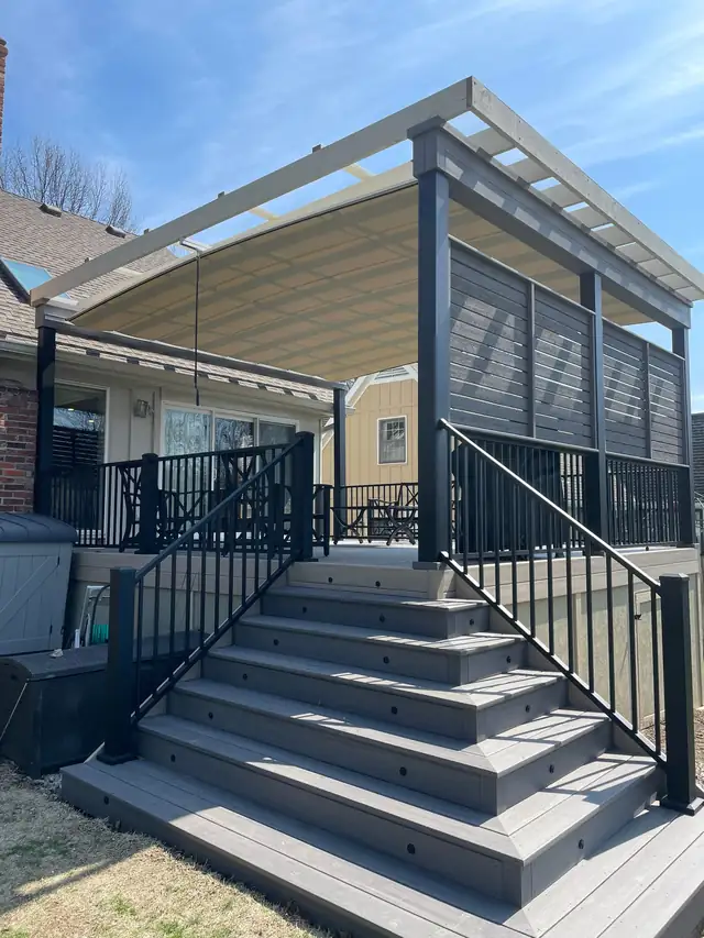 Gray composite deck stairs with black railing and a pergola privacy screen