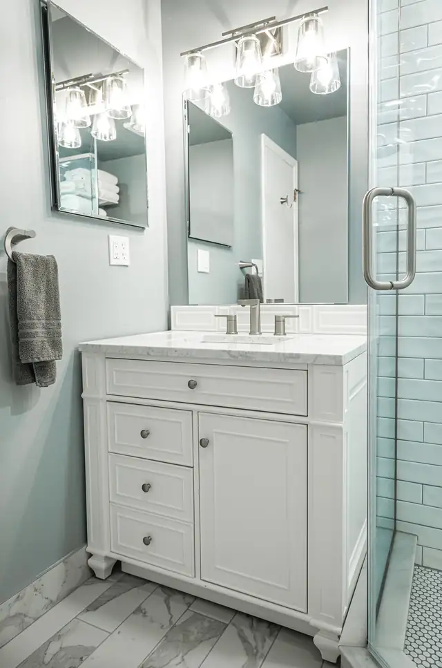 Remodeled Kansas City area bathroom with a white furniture-style vanity, marble-look top, glass shower door and gray-blue walls