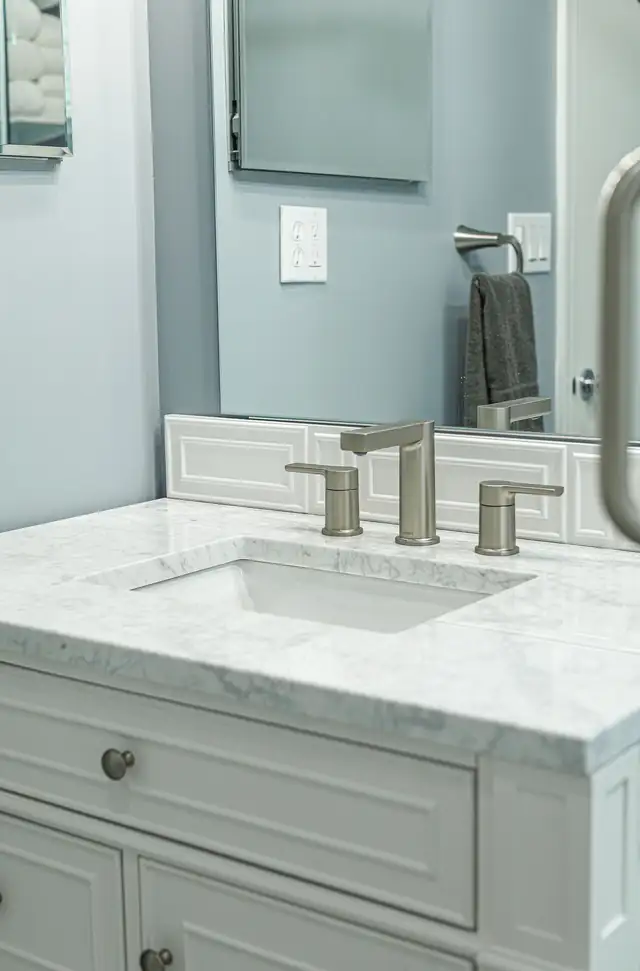 Close view of a white bathroom vanity with marble-look top and brushed nickel faucet