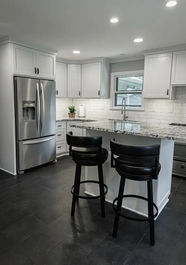 White kitchen remodel with granite island, black counter stools and dark tile floor