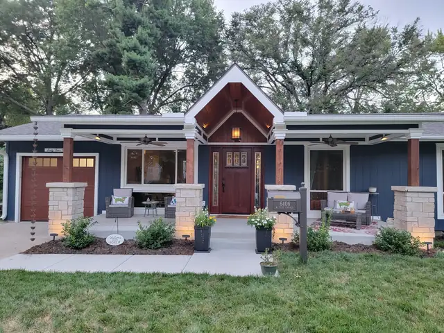 1960s ranch after a whole-home renovation with a new gabled porch, cedar posts, stone columns and blue board-and-batten siding